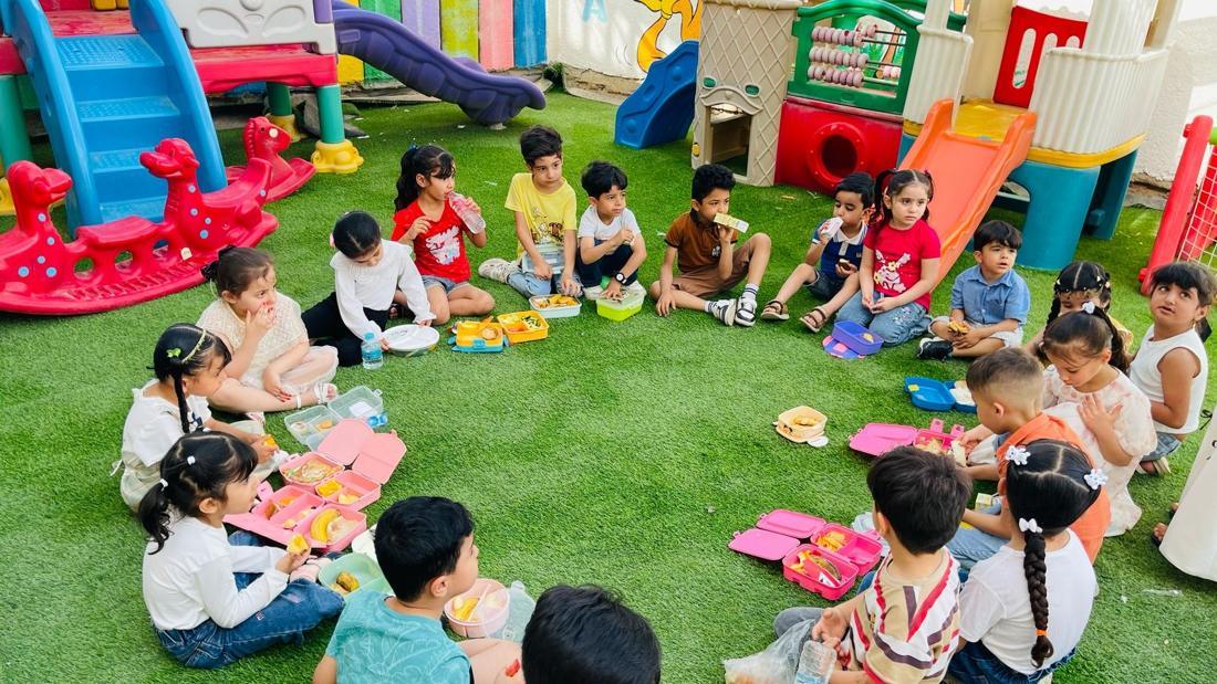 أطفال المركز يتناولون طعاماً صحياً في حلقة على العشب